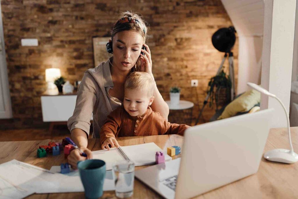 Mãe trabalhadora em teleconferência de home office com o filho ao lado, ilustrando redução de jornada para mãe de autista