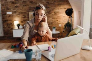 Mãe trabalhadora em teleconferência de home office com o filho ao lado, ilustrando redução de jornada para mãe de autista